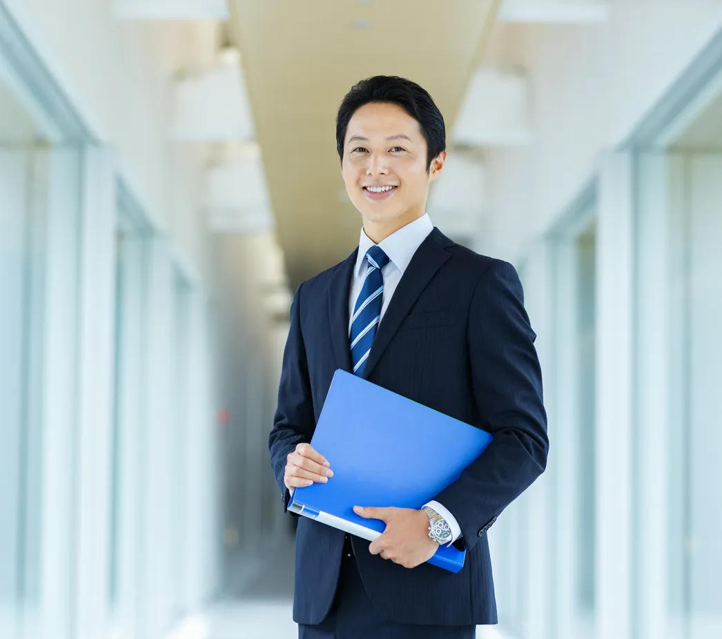 青いファイルを持って微笑むスーツ姿の男性