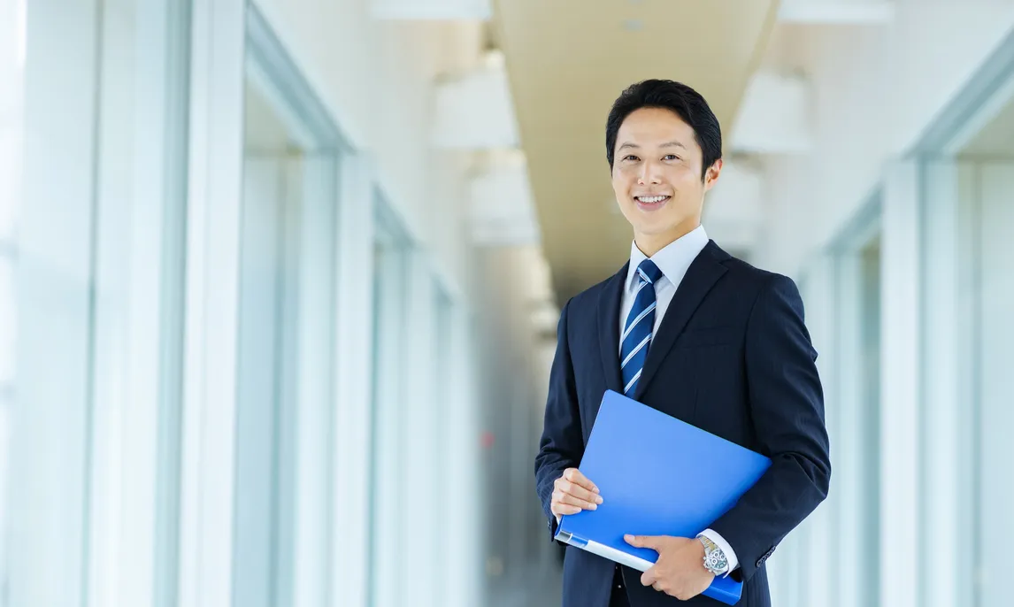 青いファイルを持って微笑むスーツ姿の男性
